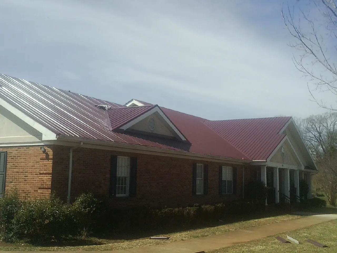 Red metal roof with gabled entries on a long brick building, from a Hail Damage Roof Repair job in Woodbury