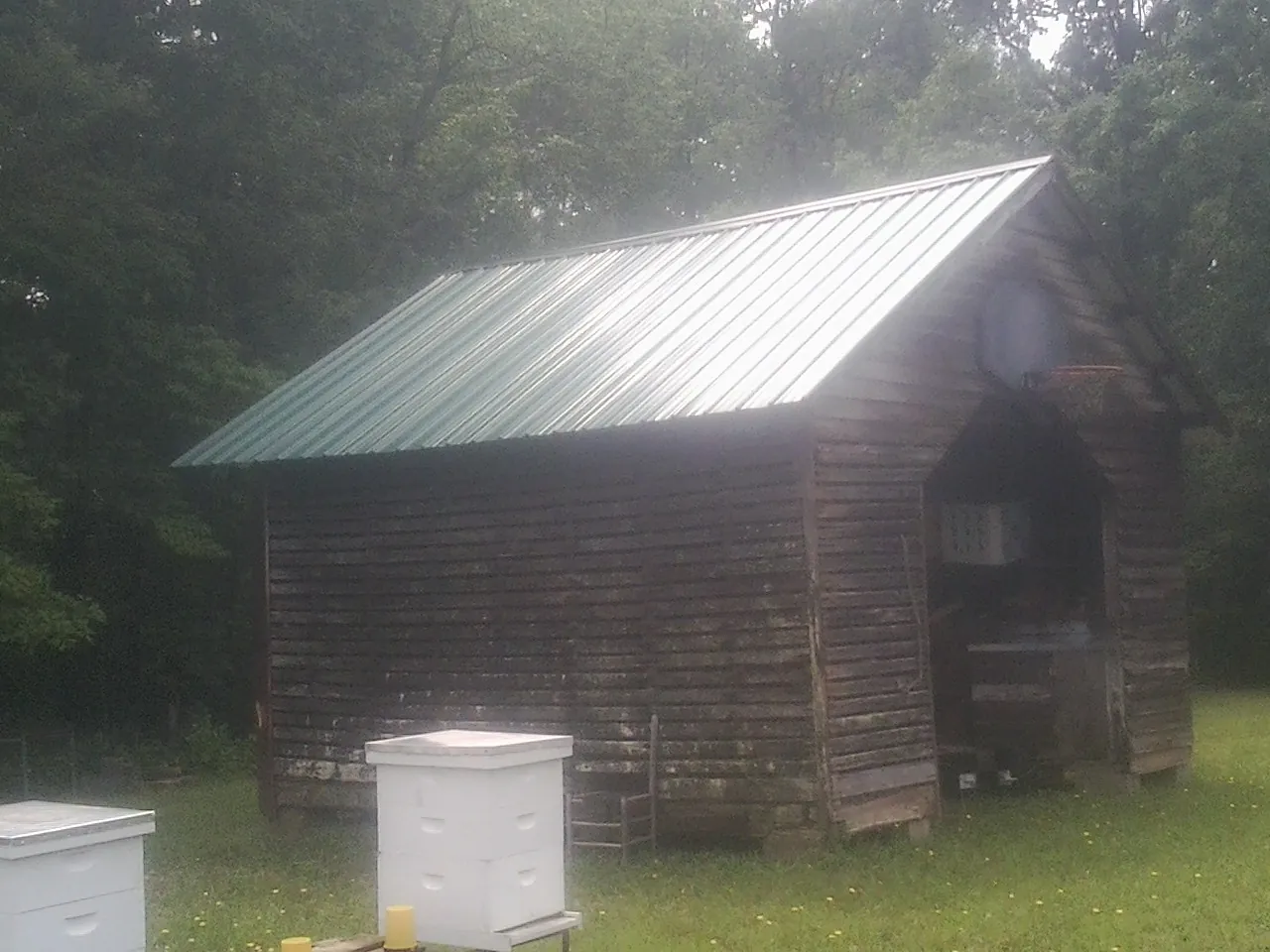 Green metal roof on a weathered barn beside stacked beehives in Woodbury